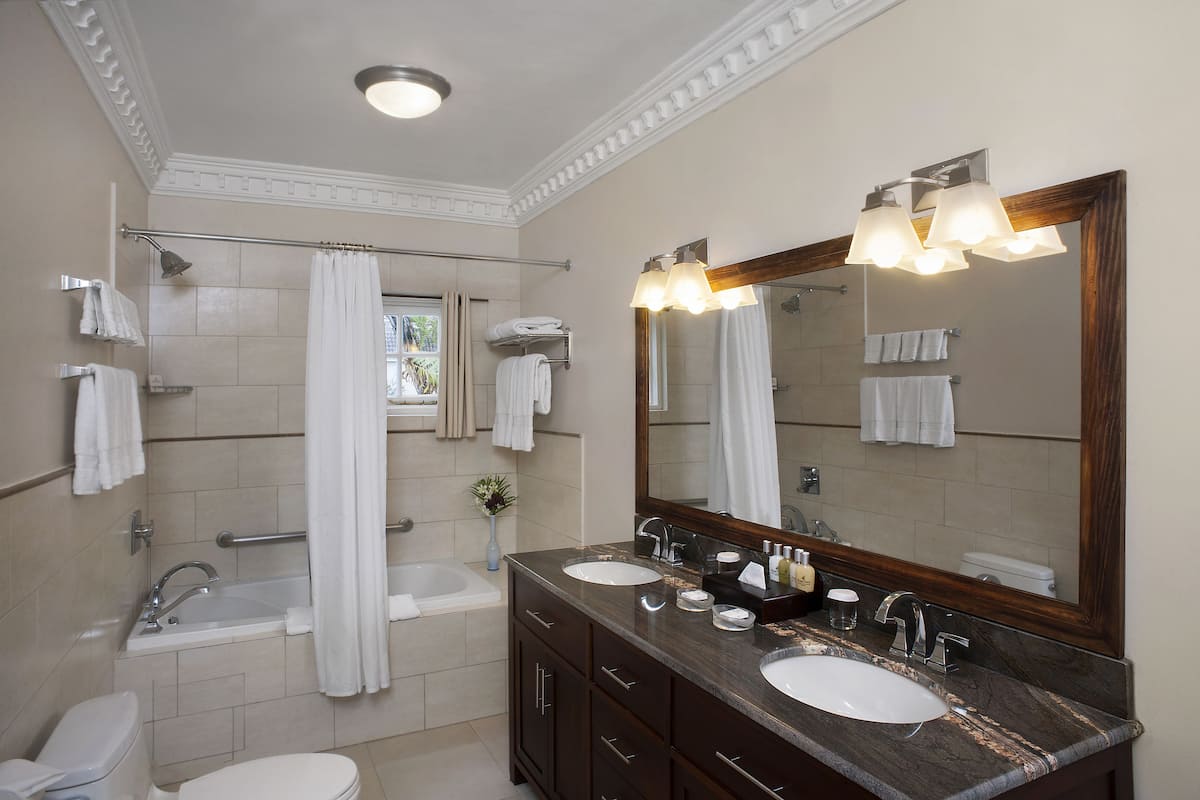 Une salle de bain moderne avec une baignoire, deux lavabos, un grand miroir et un rideau de douche.