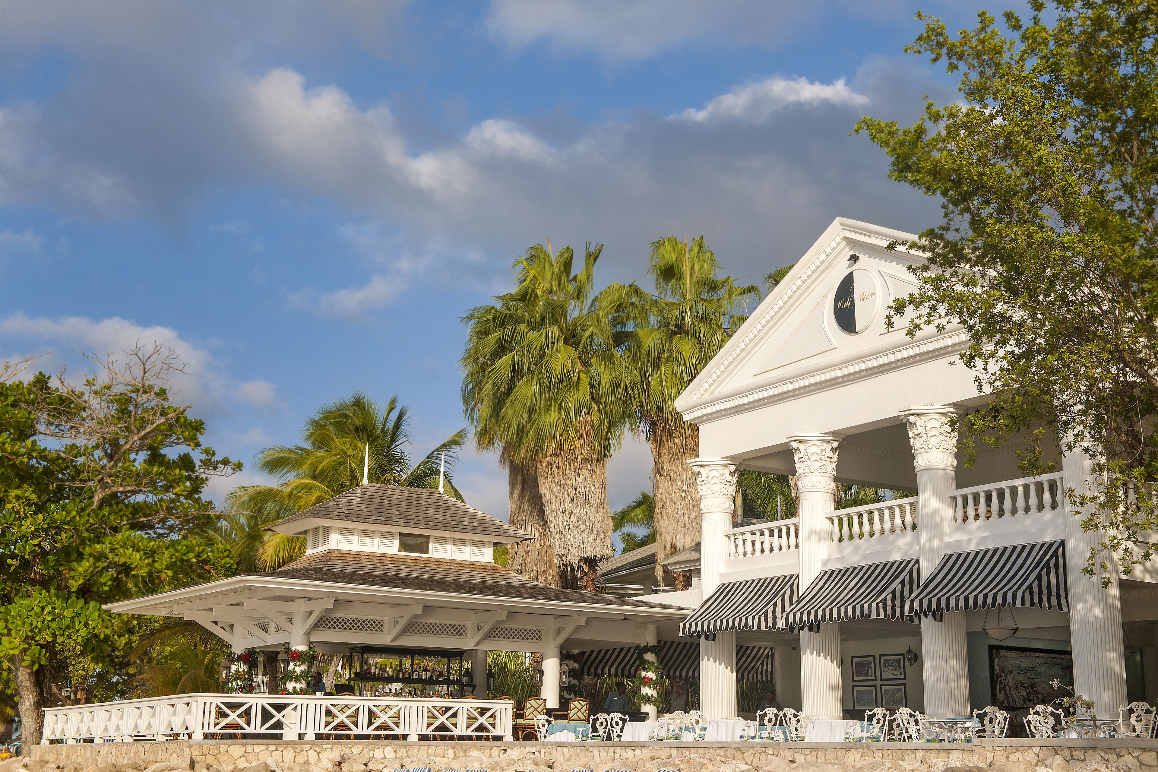 A white building with a covered patio area, palm trees, and a clear sky.