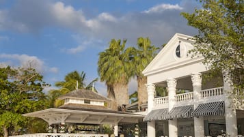 A white building with a covered patio area, palm trees, and a clear sky.