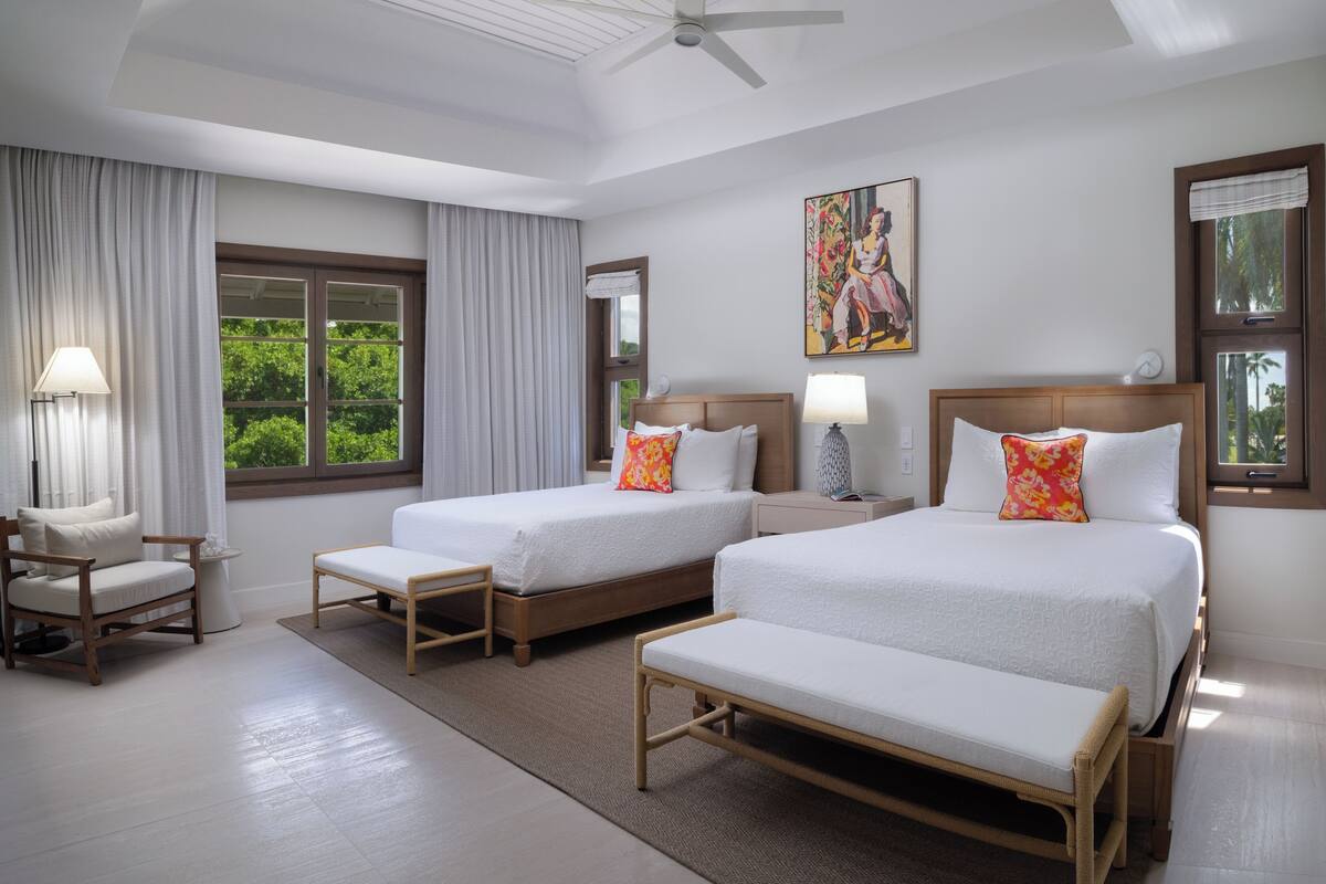 Une chambre d’hôtel avec deux lits, une chaise, une table de chevet, une lampe et un tableau au mur.
