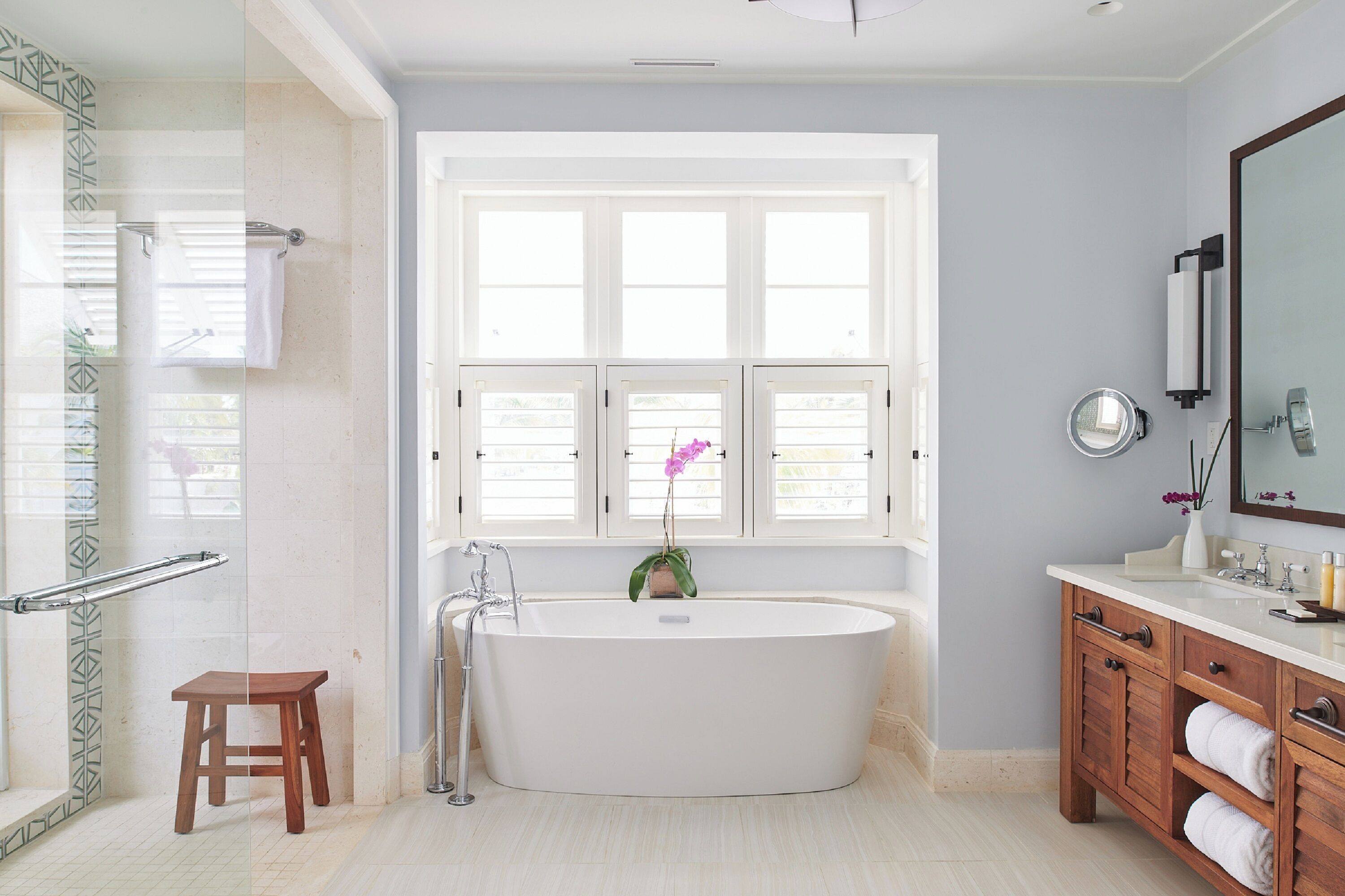 Un baño moderno con una bañera independiente, un tocador de madera, una cabina de ducha de vidrio y un ventanal que proporciona luz natural.