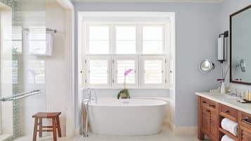 Un baño moderno con una bañera independiente, un tocador de madera, una cabina de ducha de vidrio y un ventanal que proporciona luz natural.