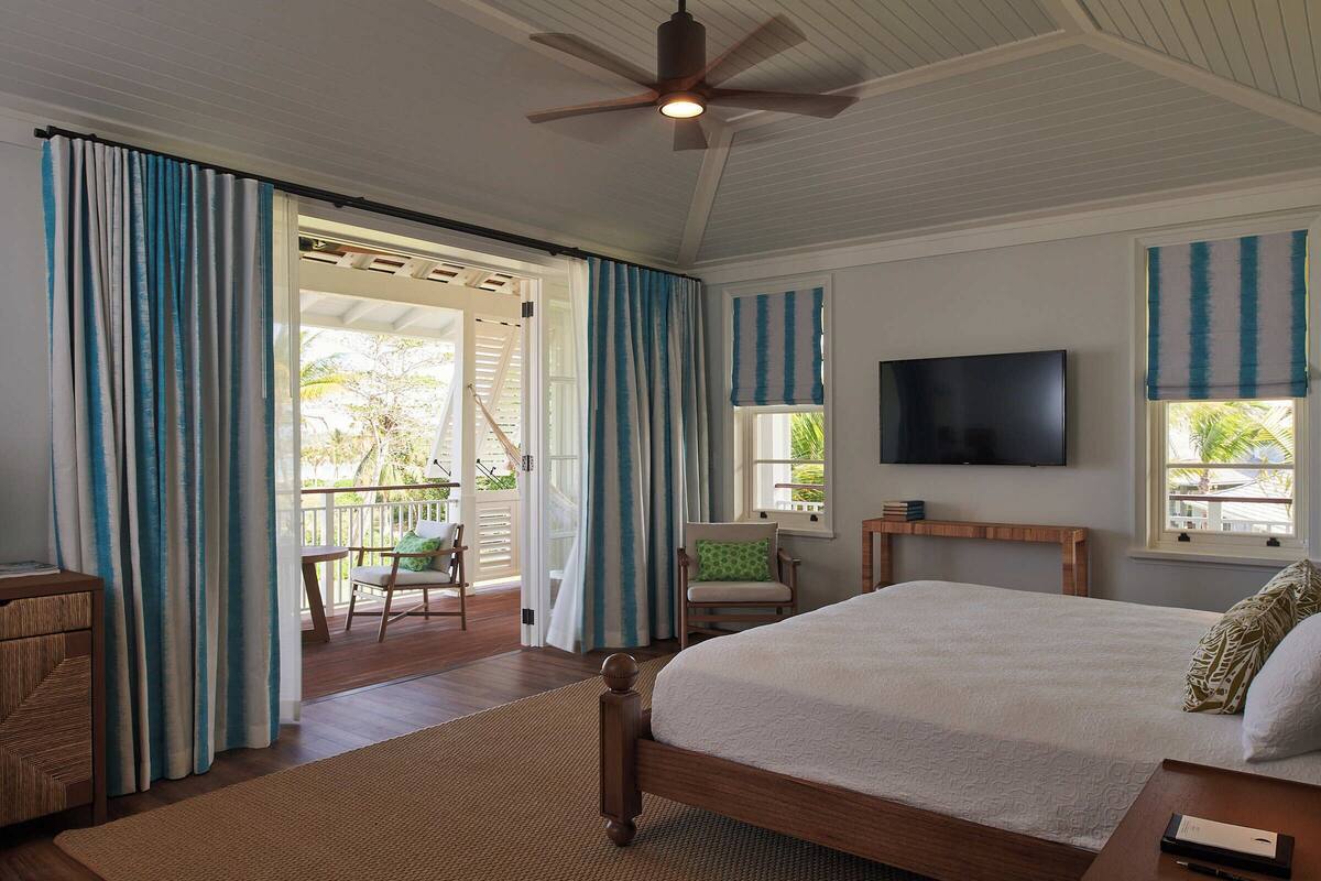 Une chambre à coucher comprenant un lit, un téléviseur, un ventilateur de plafond et une vue sur l’extérieur.