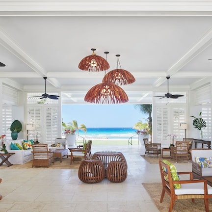A spacious living area with a view of the beach, furnished with wicker furniture and ceiling fans.