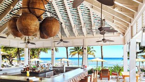 Un bar frente al mar con suelo estampado, muebles de madera y lámparas de mimbre colgantes.