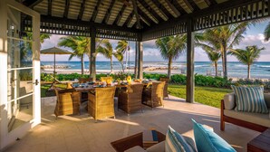 Un área de comedor al aire libre con mobiliario de mimbre, vista a la playa y un porche cubierto con vista al océano.