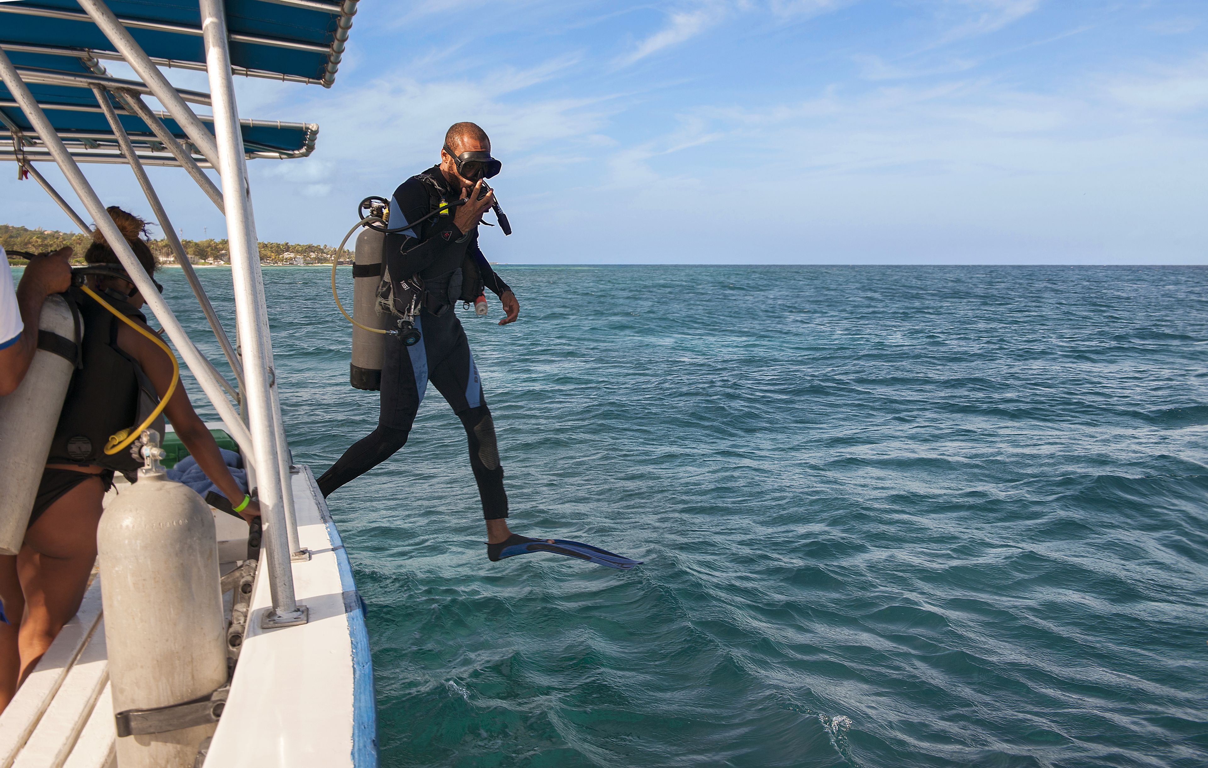 A diver in a wetsuit and fins on a boat, preparing to enter the water.