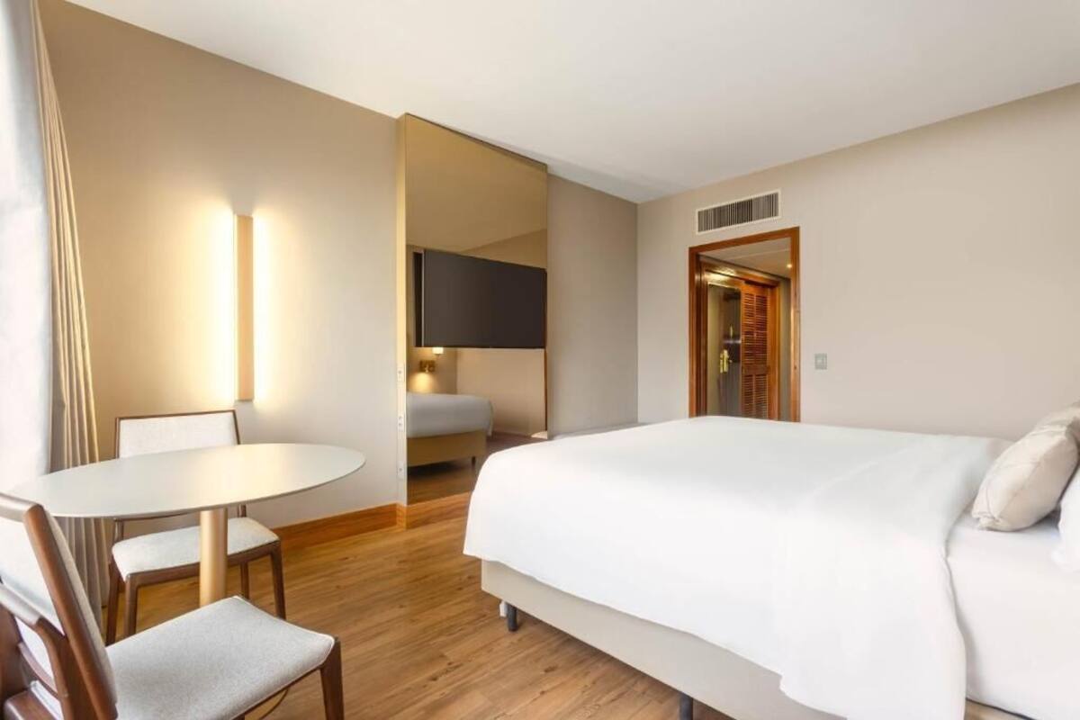Een hotelkamer met een groot bed, een ronde tafel met stoelen, een televisie en een houten vloer.