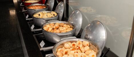 Un bufé con diversos alimentos en recipientes metálicos, incluyendo pasteles y otros platos.