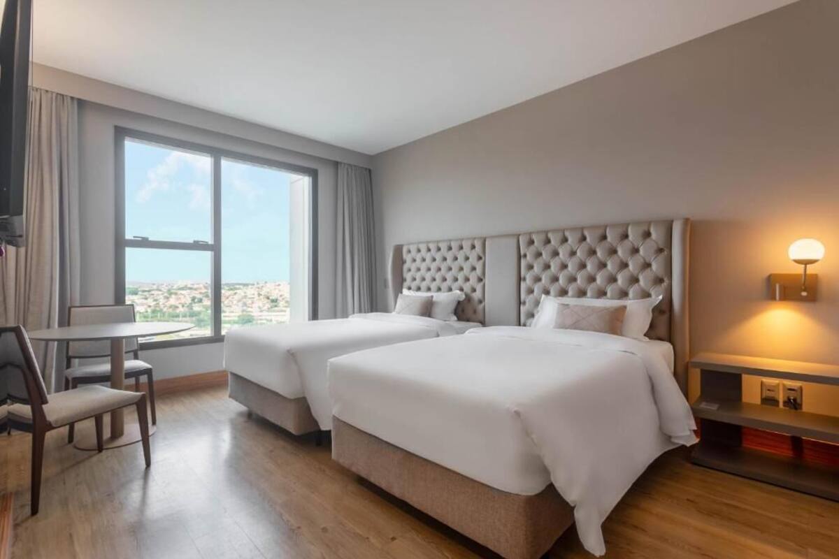 Een hotelkamer met twee bedden, een zithoek en een groot raam met uitzicht op de stad.