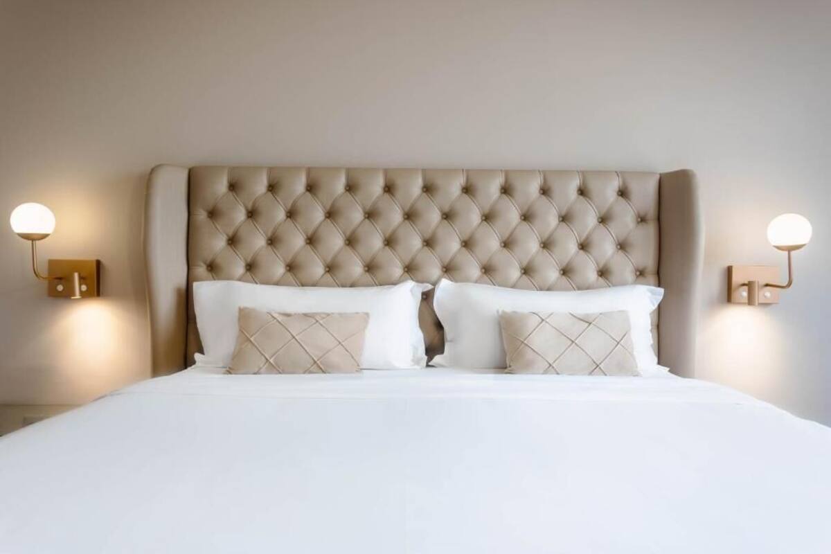 Een bed met een gestoffeerd hoofdbord, twee bedlampjes en een witte spreidekker.