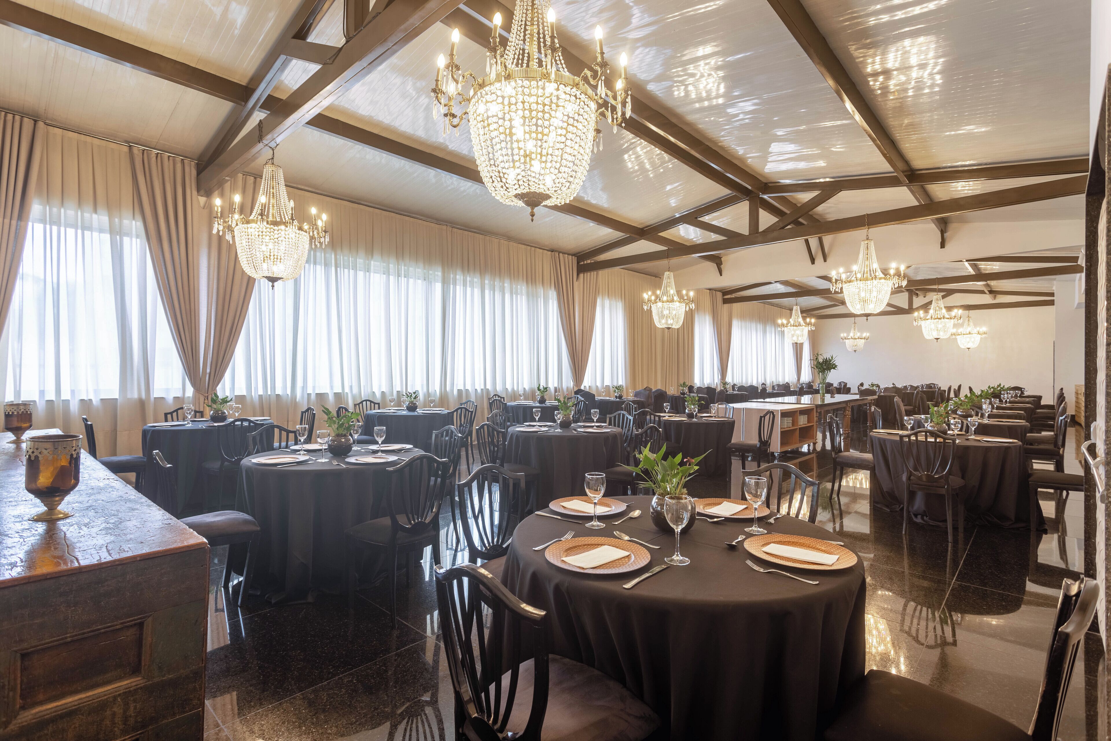 Un comedor formal con varias mesas redondas, manteles negros y elegantes candelabros.