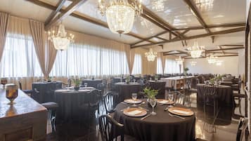 Un comedor formal con varias mesas redondas, manteles negros y elegantes candelabros.