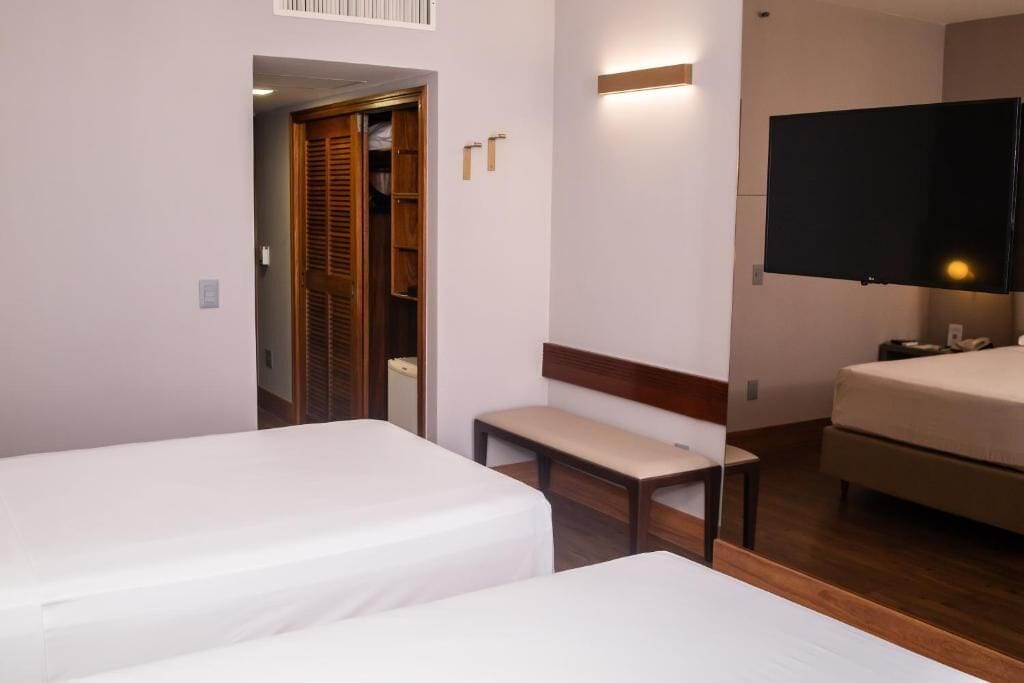 Habitación de hotel con dos camas, un banco, un televisor y un armario.