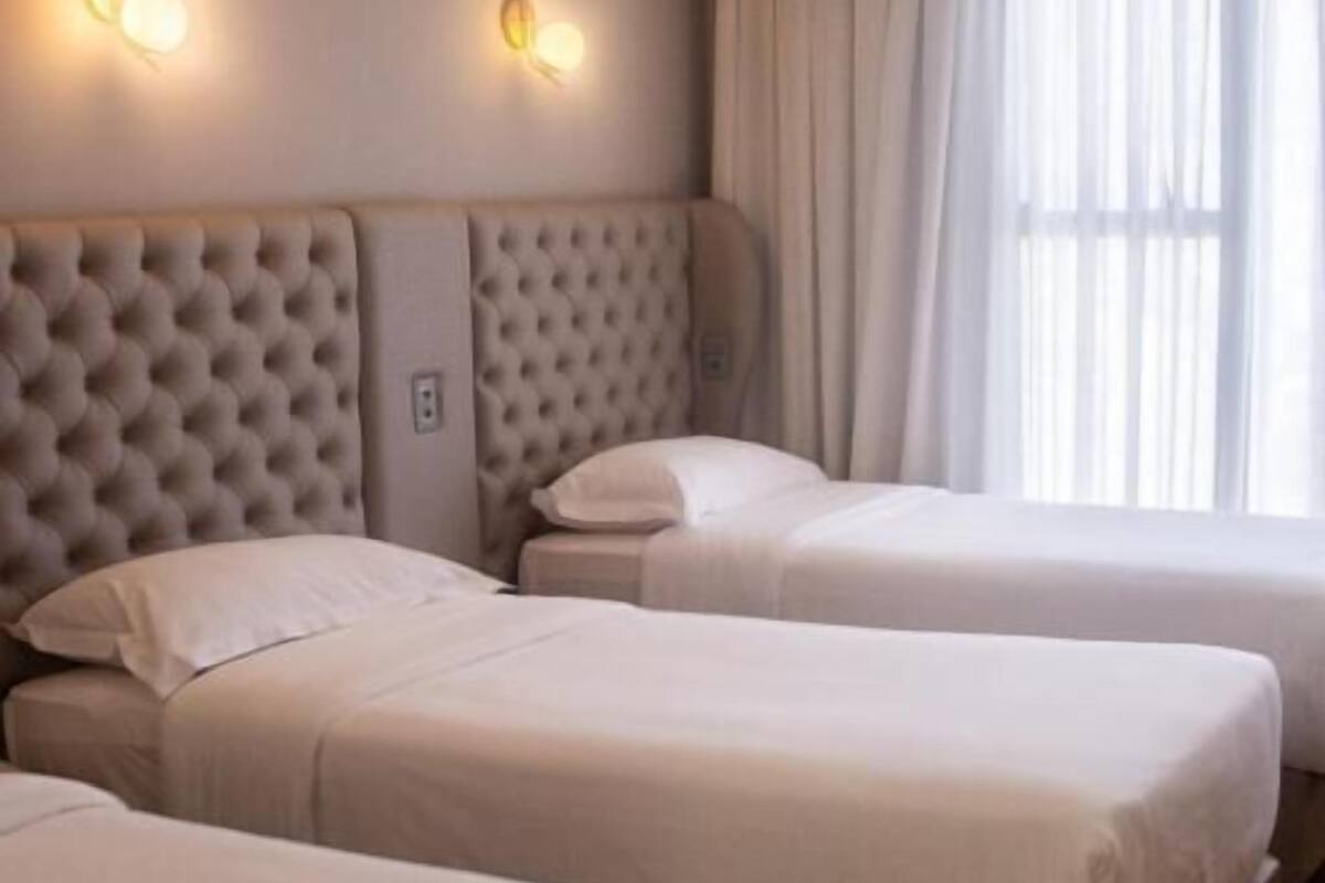 Een hotelkamer met twee bedden, een gestoffeerd hoofdeinde en een groot raam met gordijnen.
