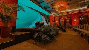 Un hall d’hôtel doté d’un grand écran diffusant une image panoramique, d’espaces aménagés pour s’asseoir et d’un plafond décoratif.