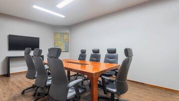 Uma sala de conferências com mesa de madeira, cadeiras pretas, TV de tela plana e um quadro abstrato colorido na parede.