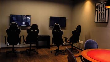 Ett konferensrum med fyra svarta spelstolar, två platt-tv-apparater som är monterade på väggen, ett träbord med en röd yta och en inramad bild av en fotbollströja.