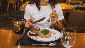 Une personne est assise à une table dans un restaurant, devant une assiette de nourriture, un verre et des couverts.
