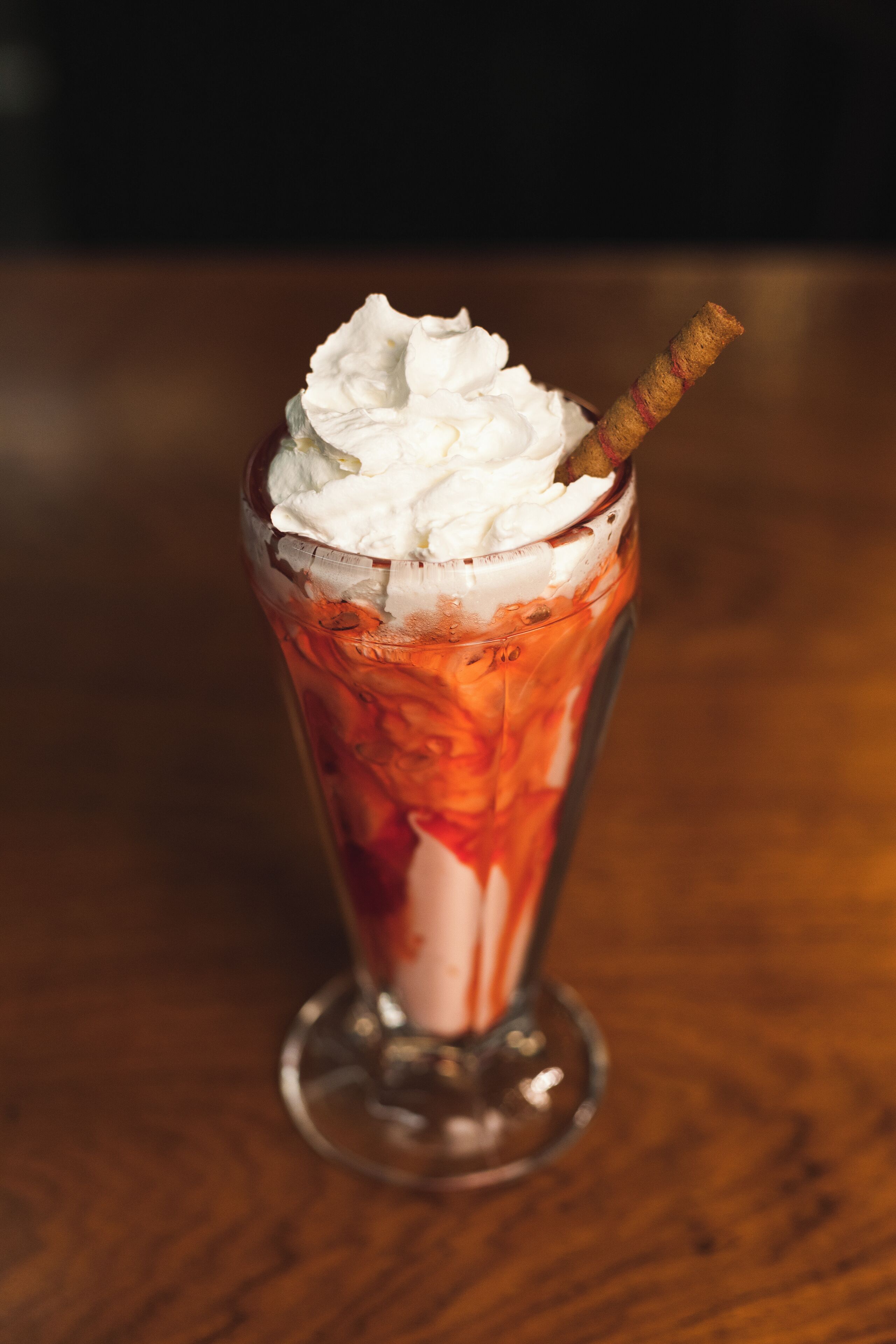 Un postre alto en vaso con crema batida y un palito de caramelo.