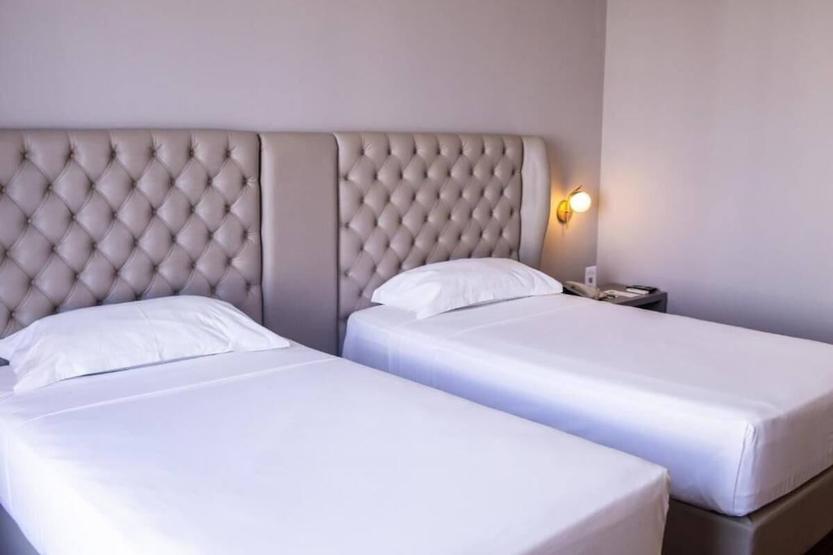Hotelkamer met twee eenpersoonsbedden, een gestapeld hoofdeinde, een nachtkastje met lamp en een wandlamp.