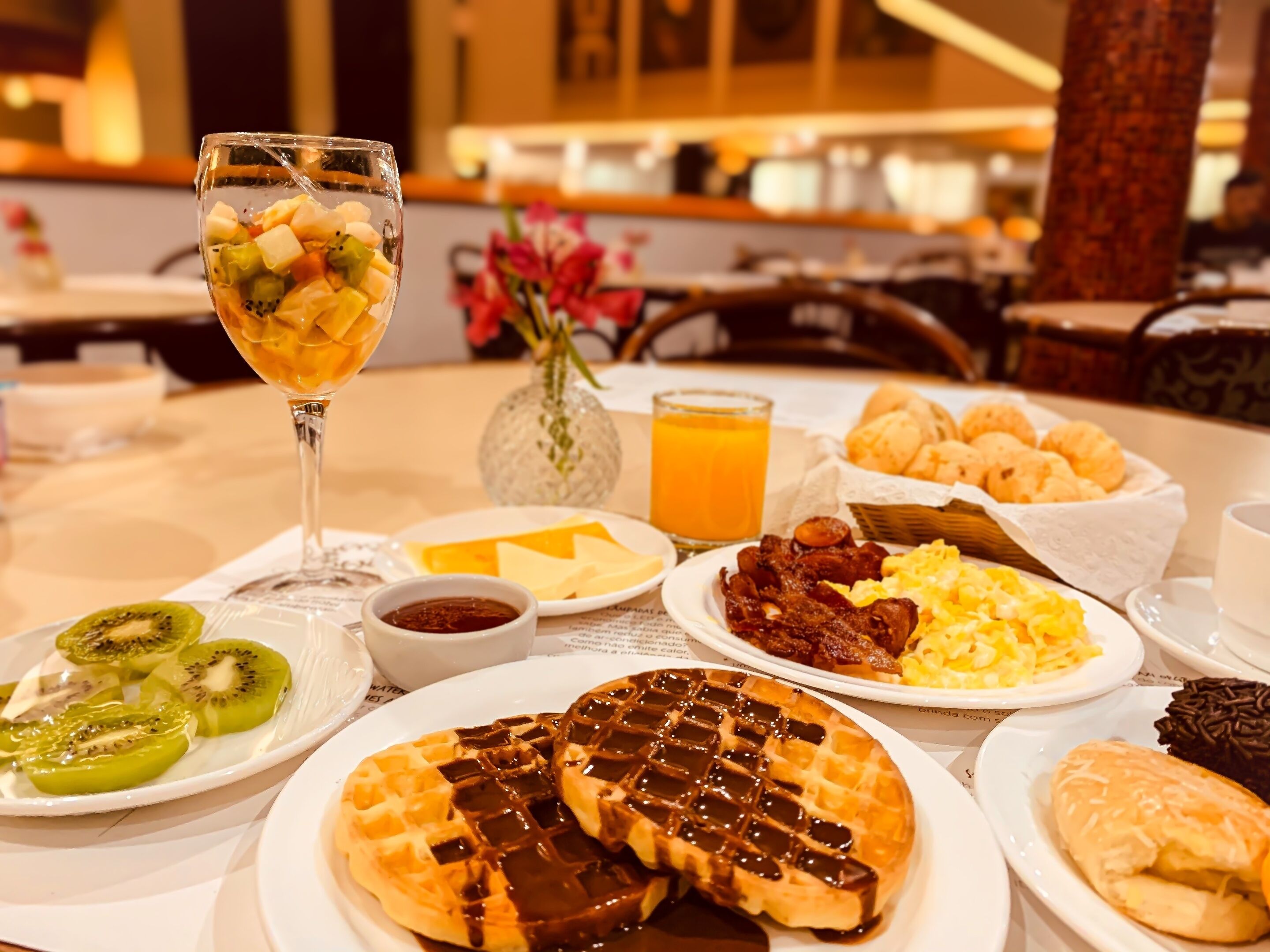 Un plateau de petit-déjeuner comprenant une variété de plats, notamment des gaufres, des œufs brouillés, du bacon et une boisson aux fruits.