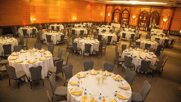 Un amplio salón de banquetes con varias mesas redondas dispuestas para recibir comensales, cada una con mantel blanco y servilletas amarillas.