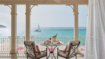 A covered outdoor seating area with a table set for two, overlooking a beach with a sailboat in the distance.