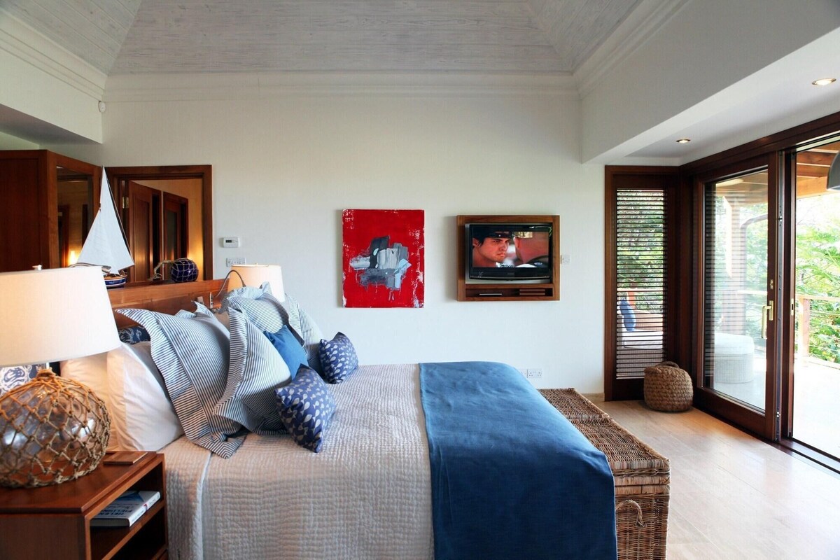A bedroom with a bed, a TV, a lamp, and a large window.