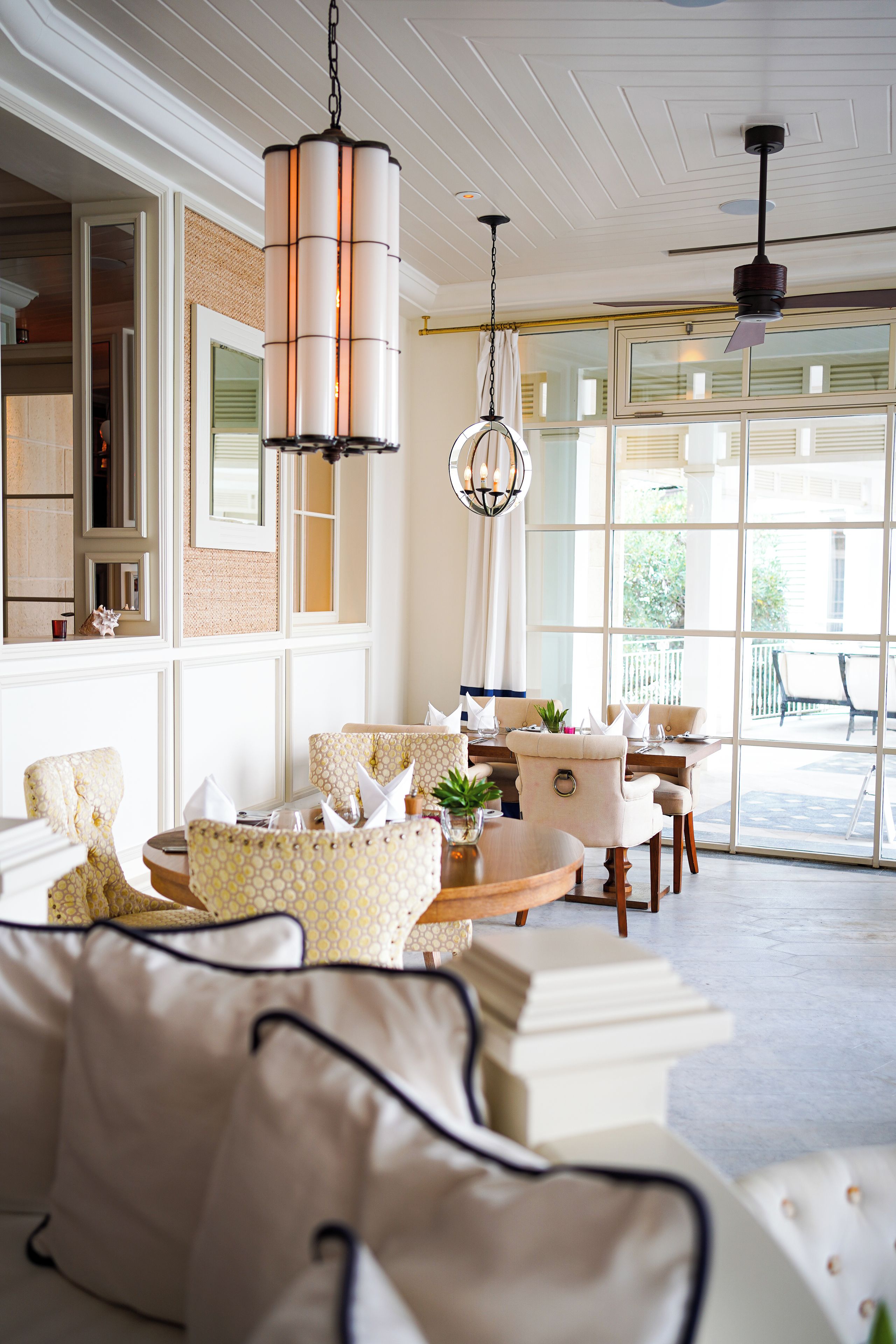 A well-lit room with a large window, a chandelier, and a dining area with chairs and a table.