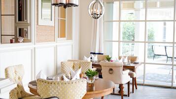 A well-lit room with a large window, a chandelier, and a dining area with chairs and a table.