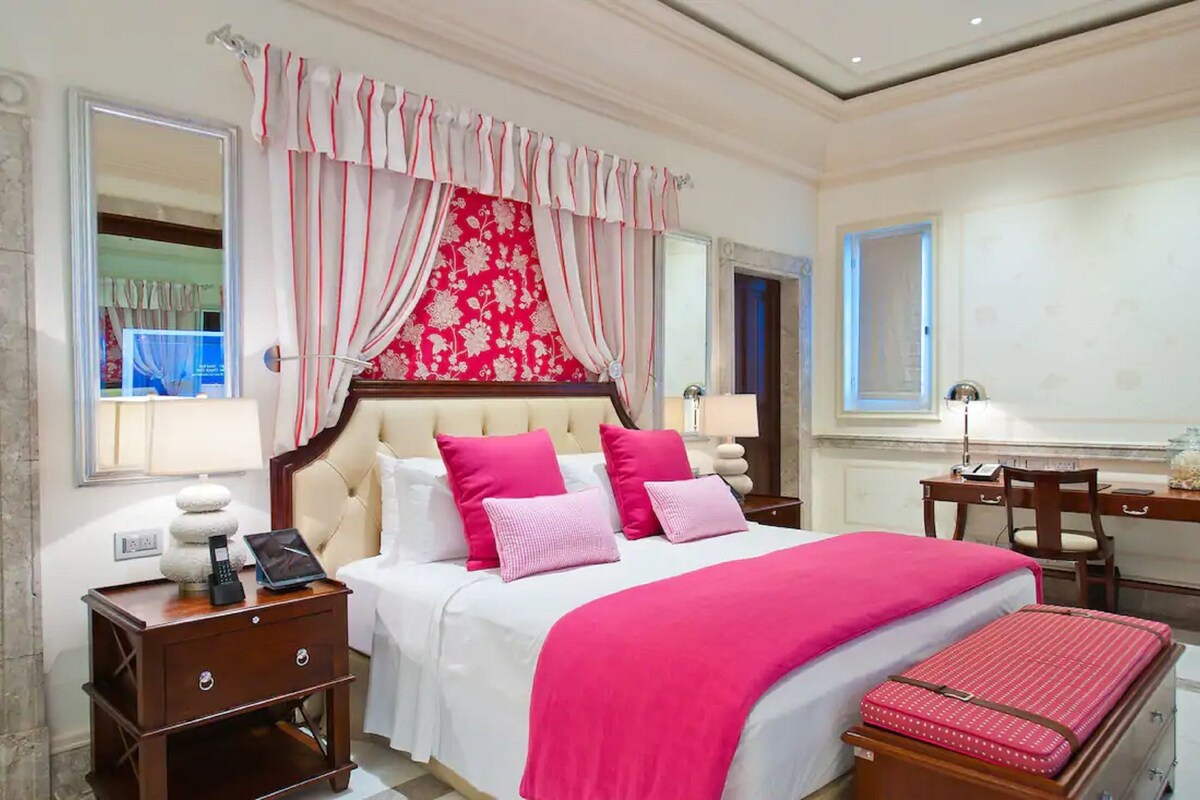 Una habitación de hotel con una cama grande, un escritorio, una silla, una mesita de noche y una maleta.