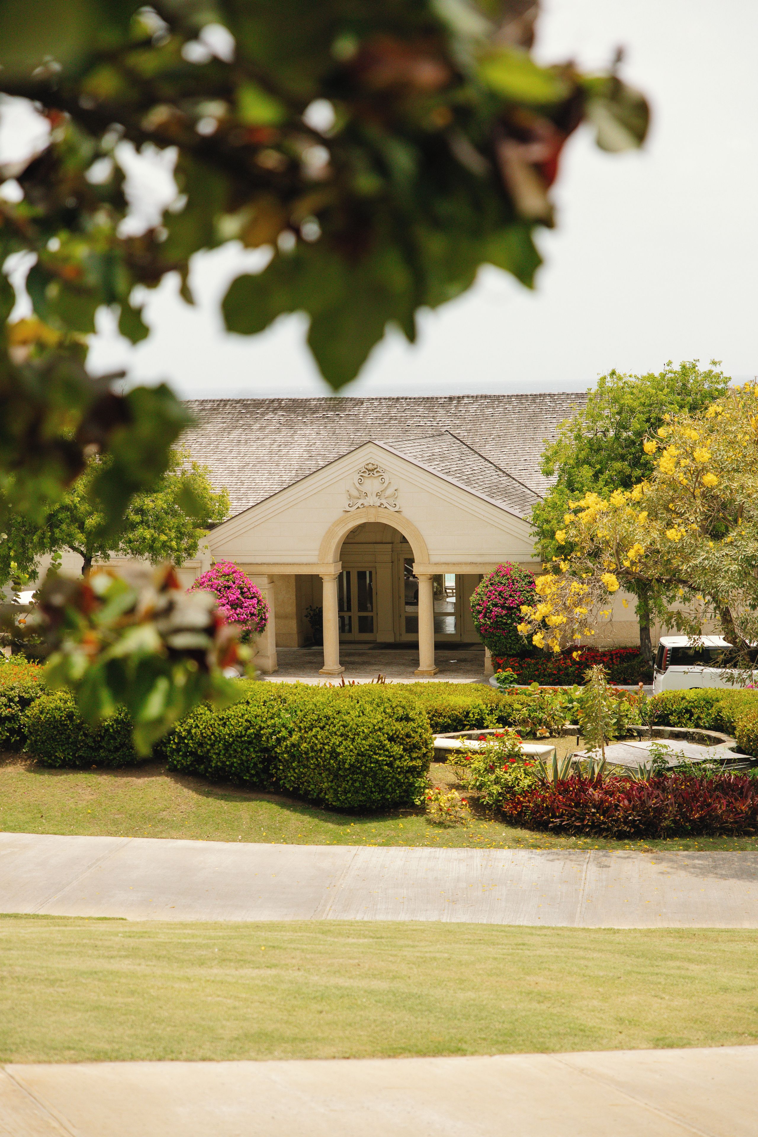 A building with a central entrance, surrounded by well-maintained gardens and a paved pathway.
