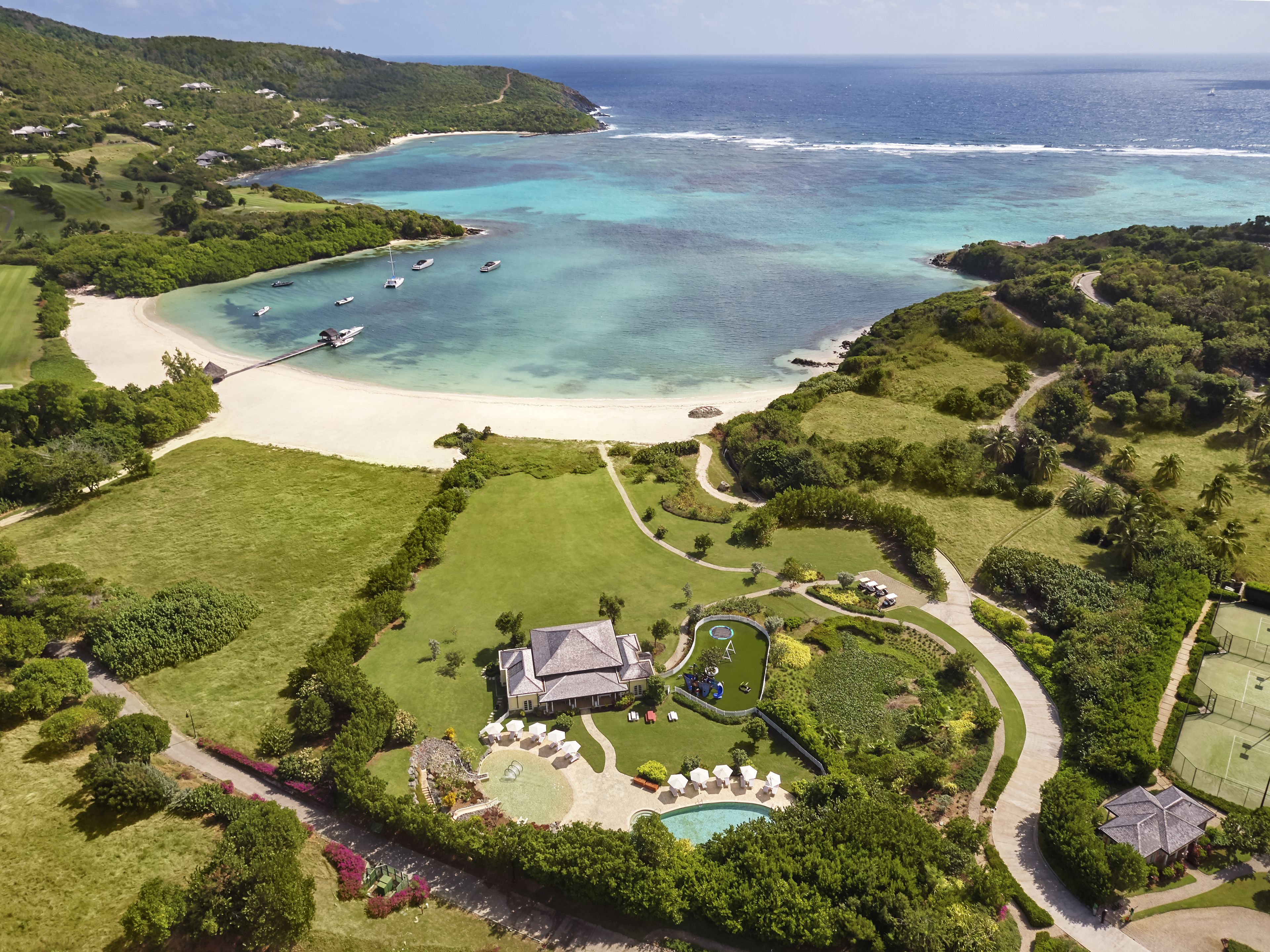 An aerial view of a coastal property with a beach, a swimming pool, and a tennis court.