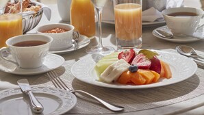 A table set with breakfast items, including fruit, juice, and a bottle of champagne, with a view of the sea and a sailboat in the background. - Mandarin Oriental, Canouan (Canouan Island)