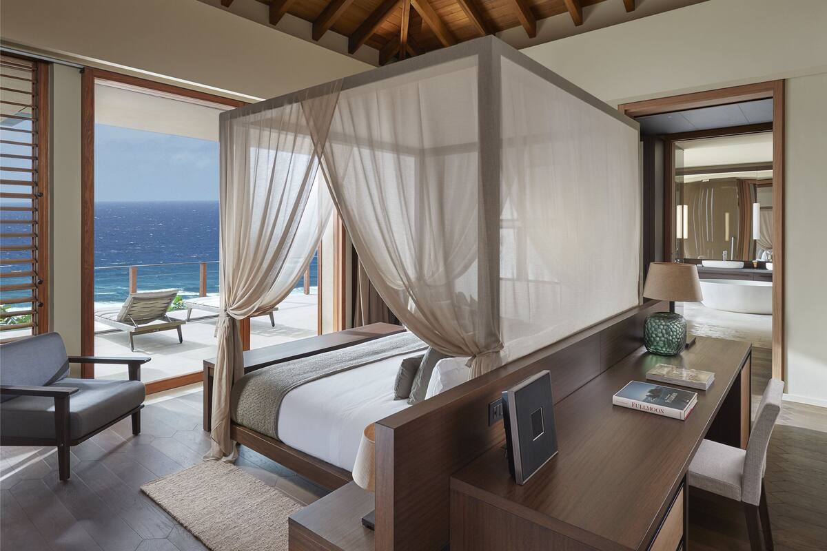 Un dormitorio con una cama grande, un escritorio y vista al océano.