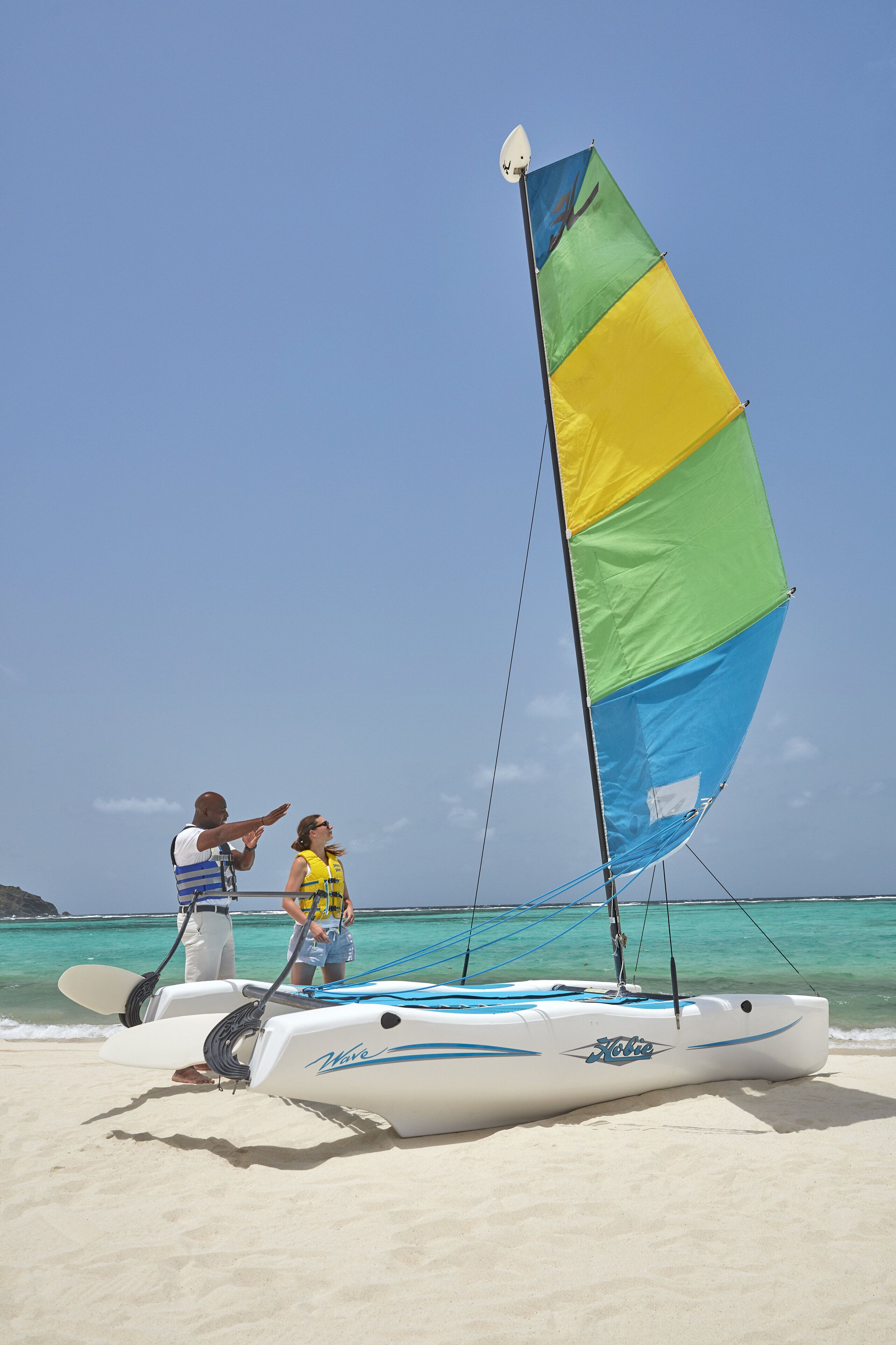 A beach with a sailboat, a person pointing at the boat, and another person standing nearby.