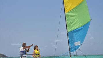 A beach with a sailboat, a person pointing at the boat, and another person standing nearby.
