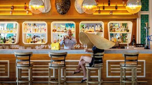 Un bar con taburetes de madera, una mujer con sombrero de paja y estantes llenos de botellas de licor.