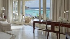 A spacious living room with a large window offering a view of the ocean. There is a ceiling fan, a sofa, and a table with chairs. - Mandarin Oriental, Canouan (Canouan Island)