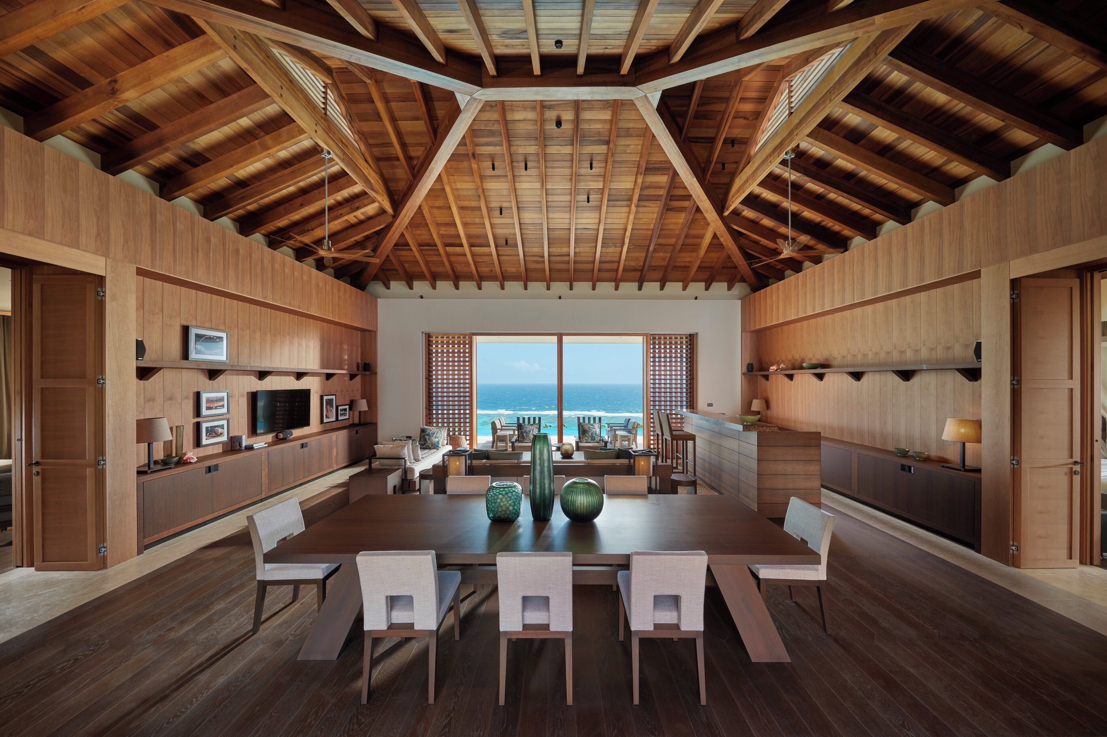 A spacious dining area with a high ceiling and wooden beams, overlooking a scenic ocean view.