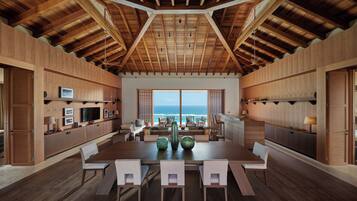 A spacious dining area with a high ceiling and wooden beams, overlooking a scenic ocean view.