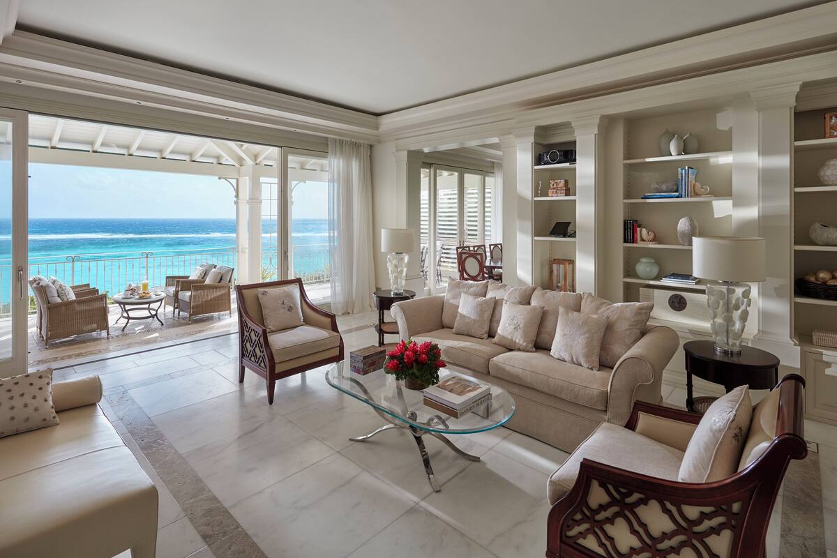 Un salón amplio con una mesa de centro de vidrio, sofás color beige y vista al océano.