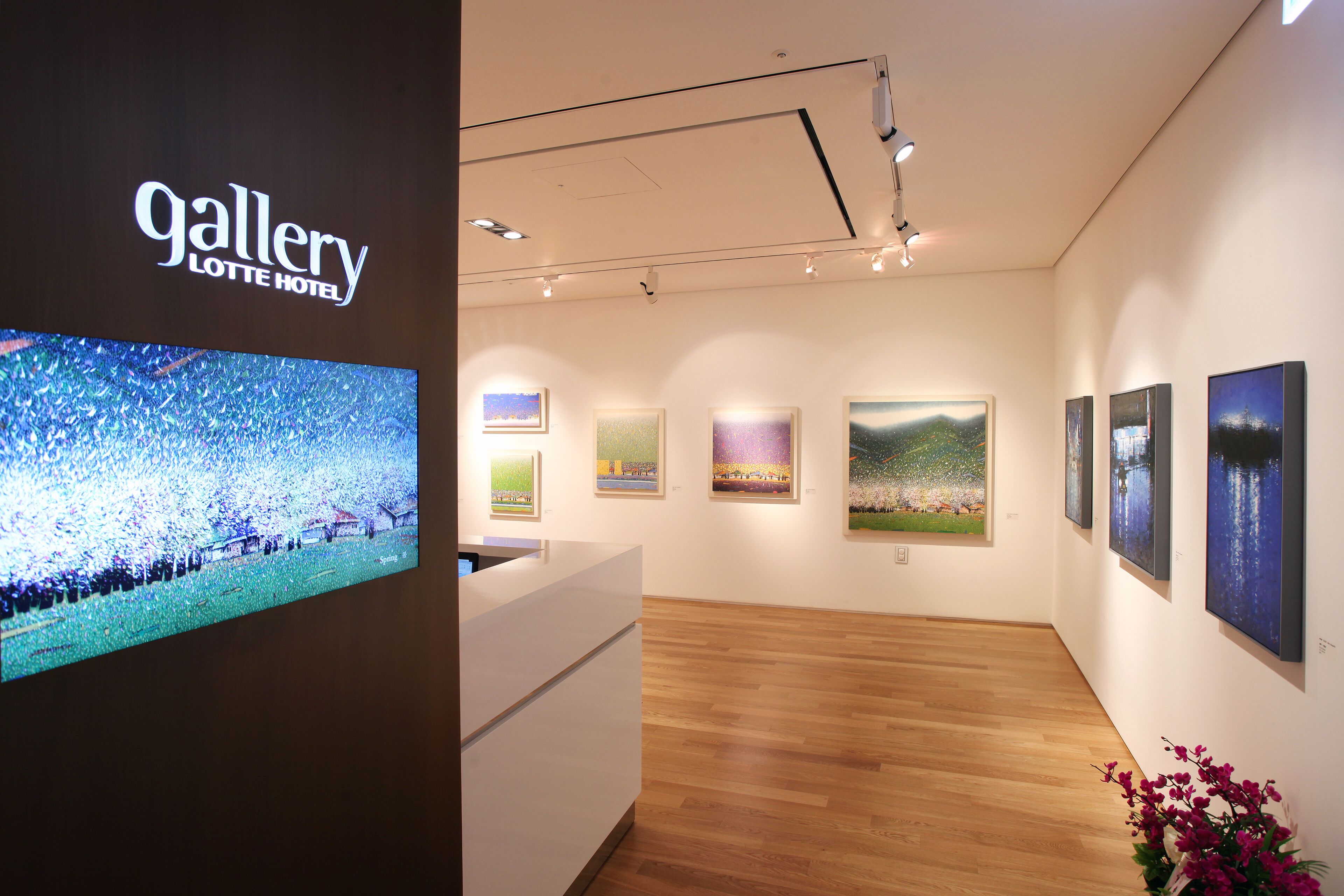 Una galería de arte con un mostrador de recepción, suelos de madera y varias pinturas en las paredes.