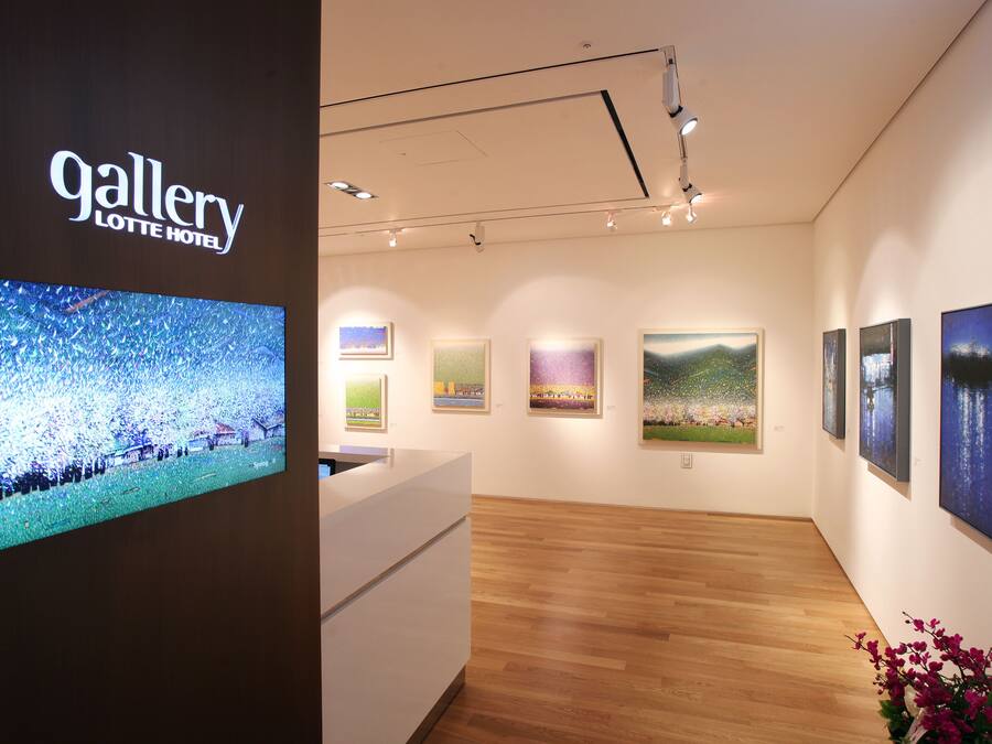 An art gallery with a reception desk, wooden floors, and various paintings on the walls.