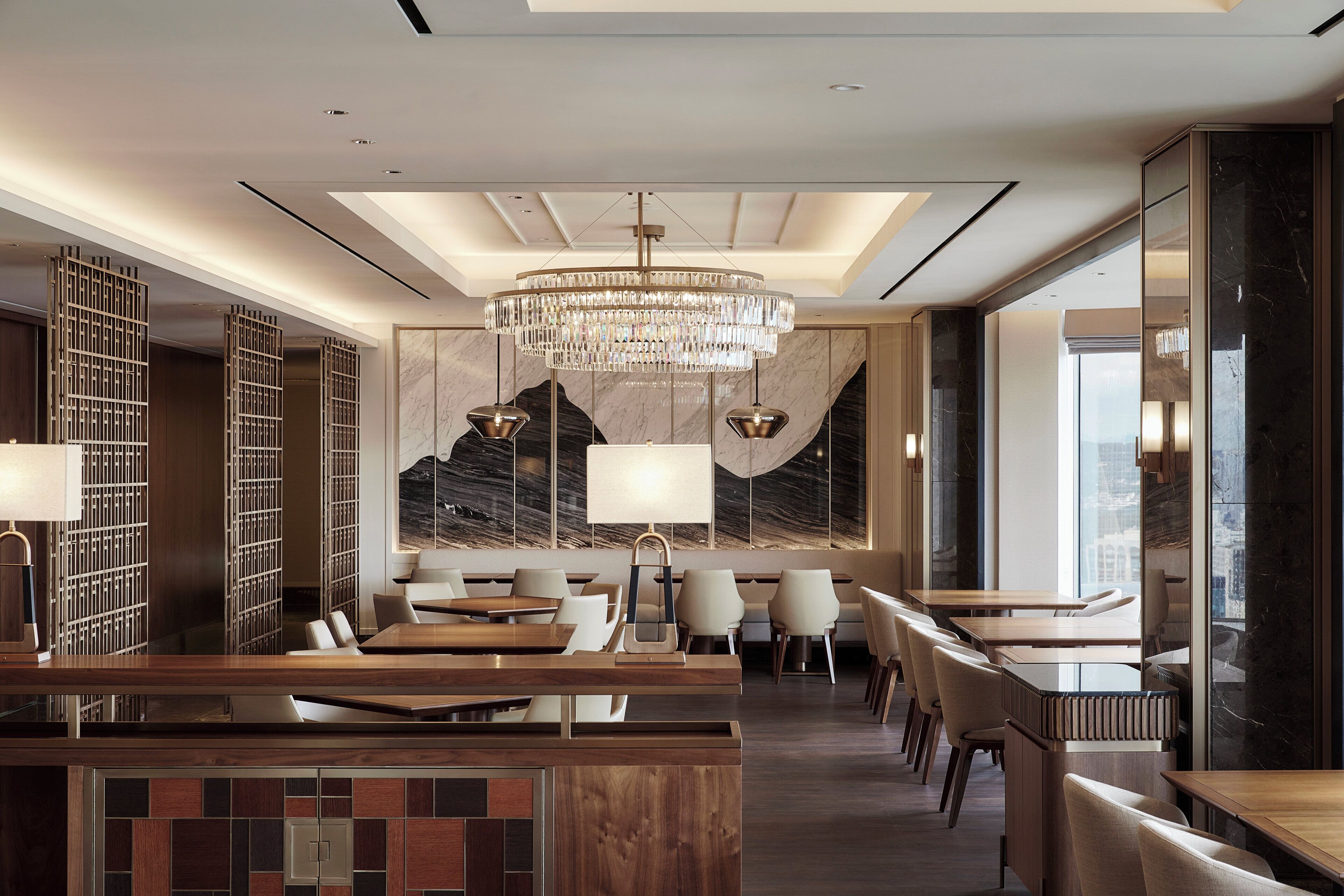 A modern restaurant with a central chandelier, wooden tables, and chairs.