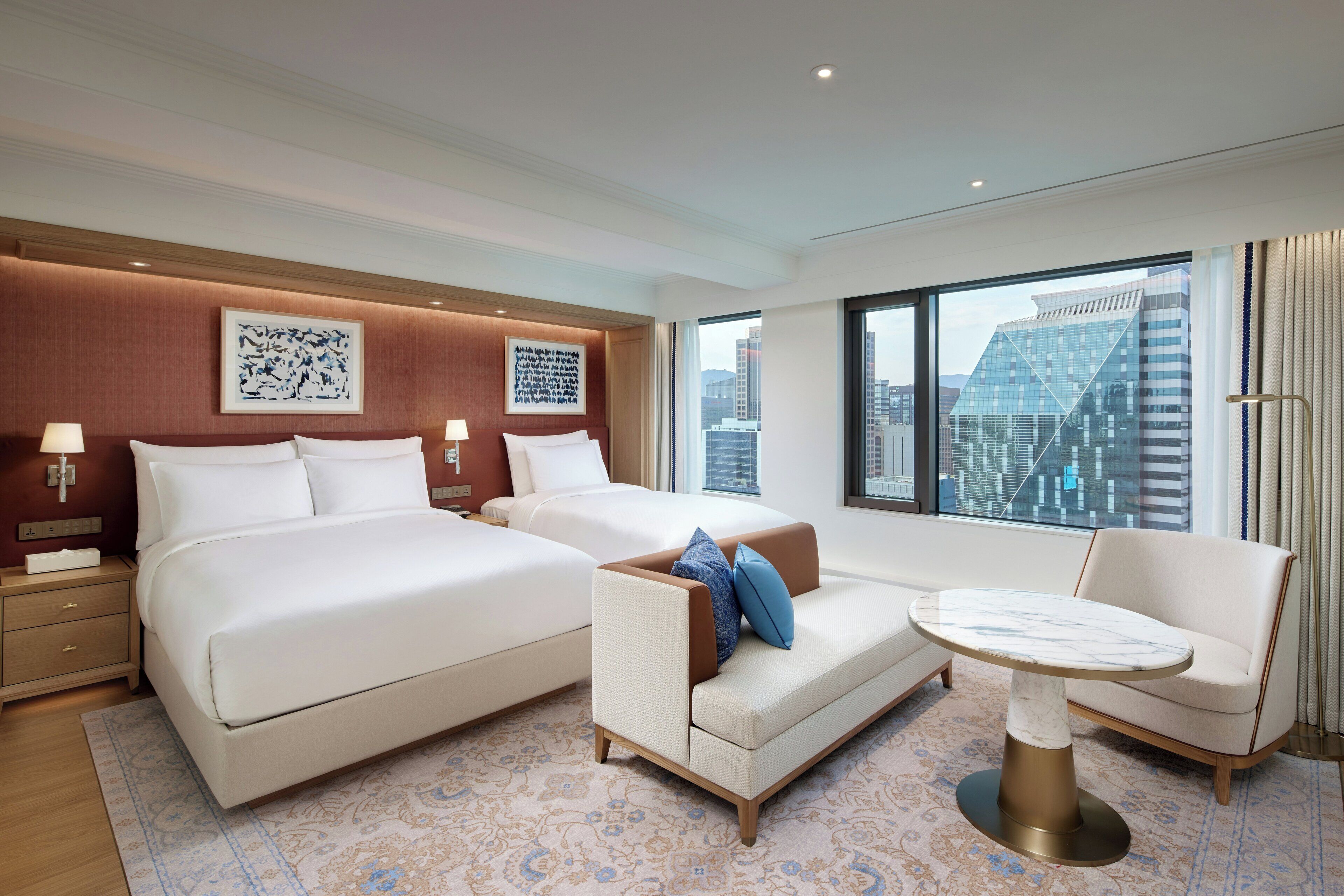 A hotel room with a large bed, a sofa, a small table, and a view of the cityscape.