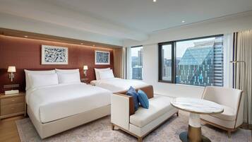 A hotel room with a large bed, a sofa, a small table, and a view of the cityscape.