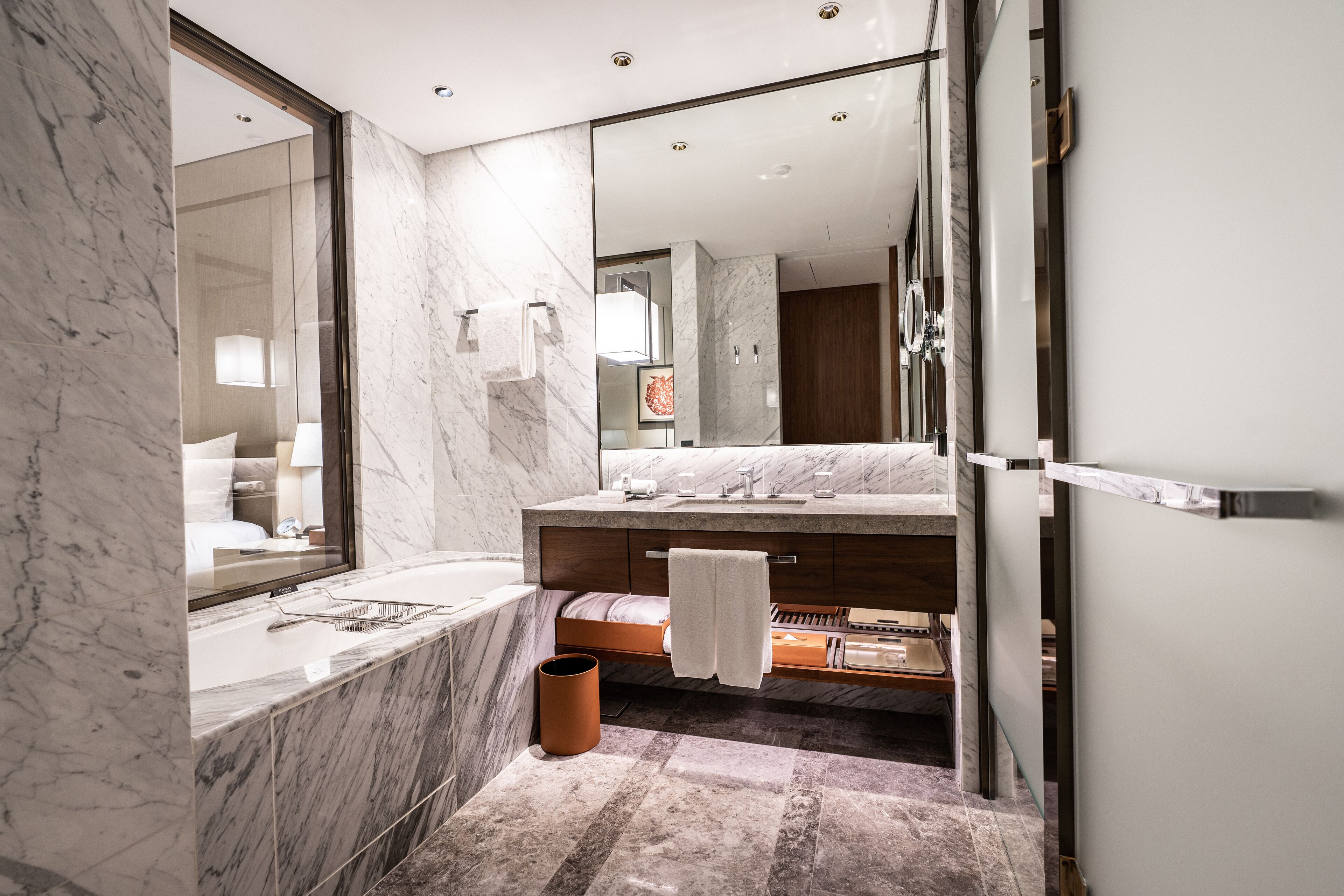 A modern bathroom with a large mirror, marble countertops, a bathtub, and a shower area.