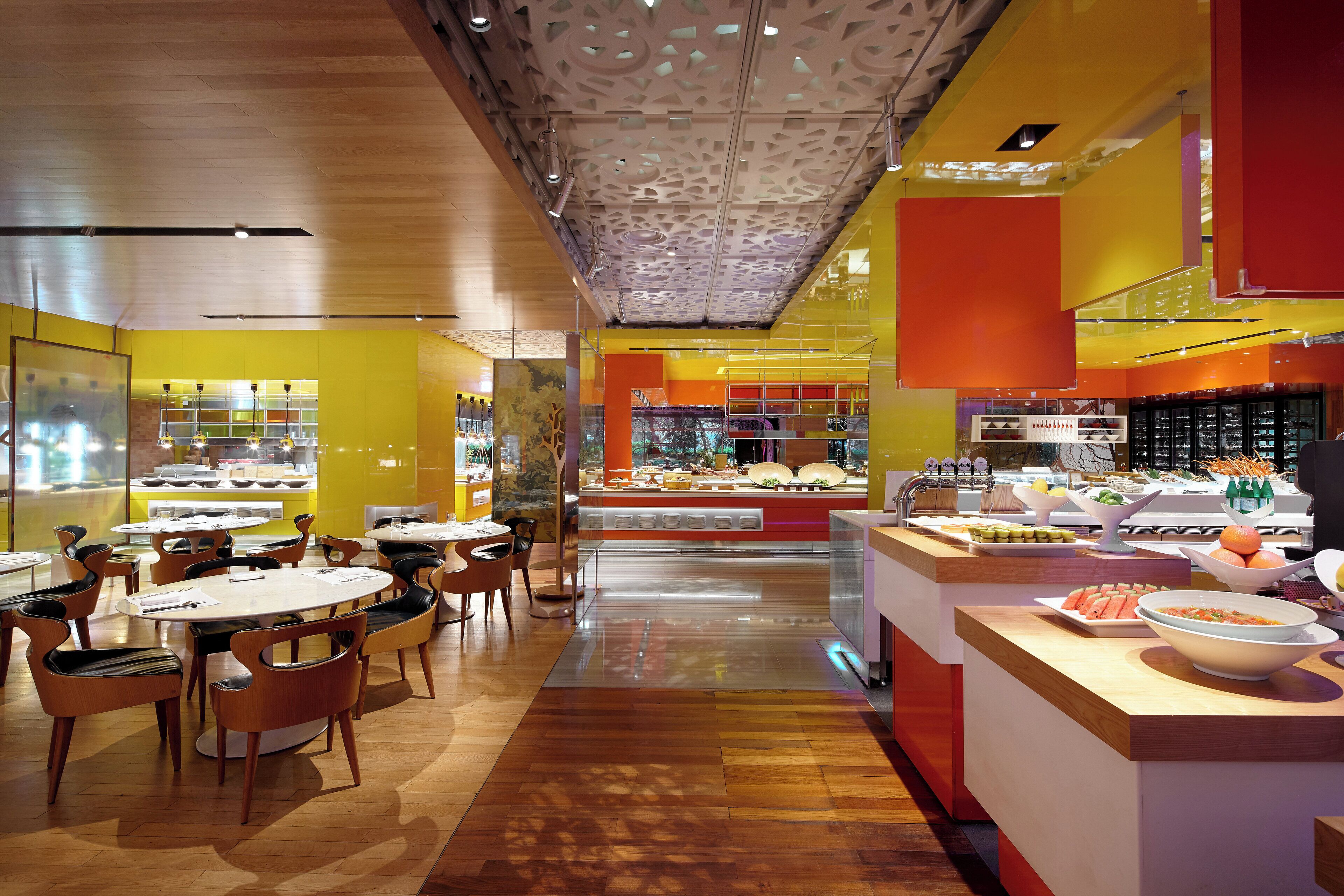 A modern restaurant interior with round tables and chairs, a central buffet area, and a bright color scheme.